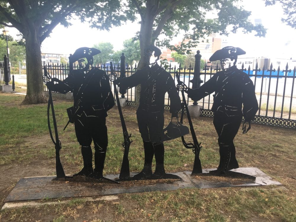 A flat metal statue that shows a silhouette of three American Minutemen. 
