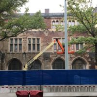 An building under restoration: it has a construction fence and a crane in front of…