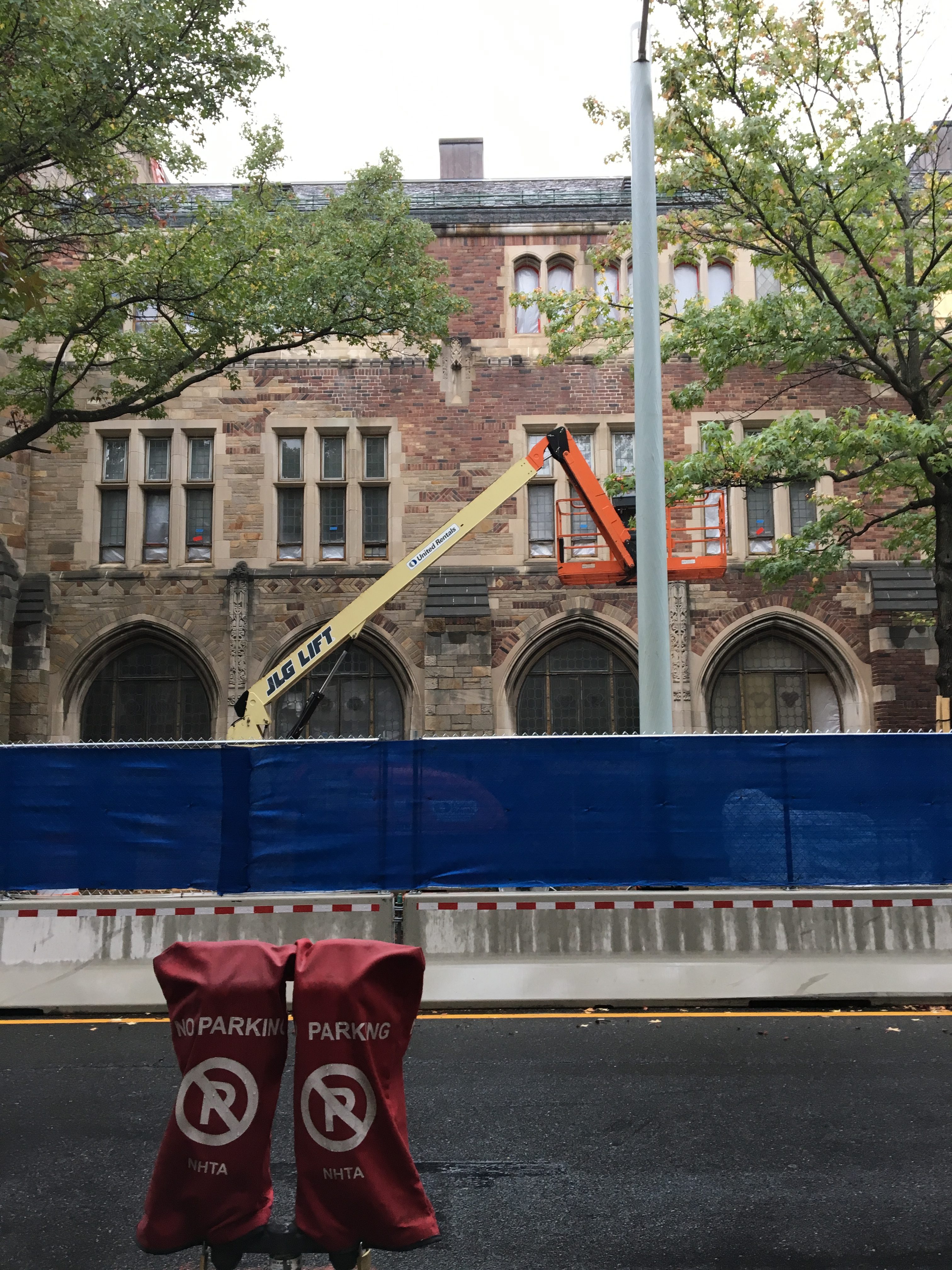 An building under restoration: it has a construction fence and a crane in front of…