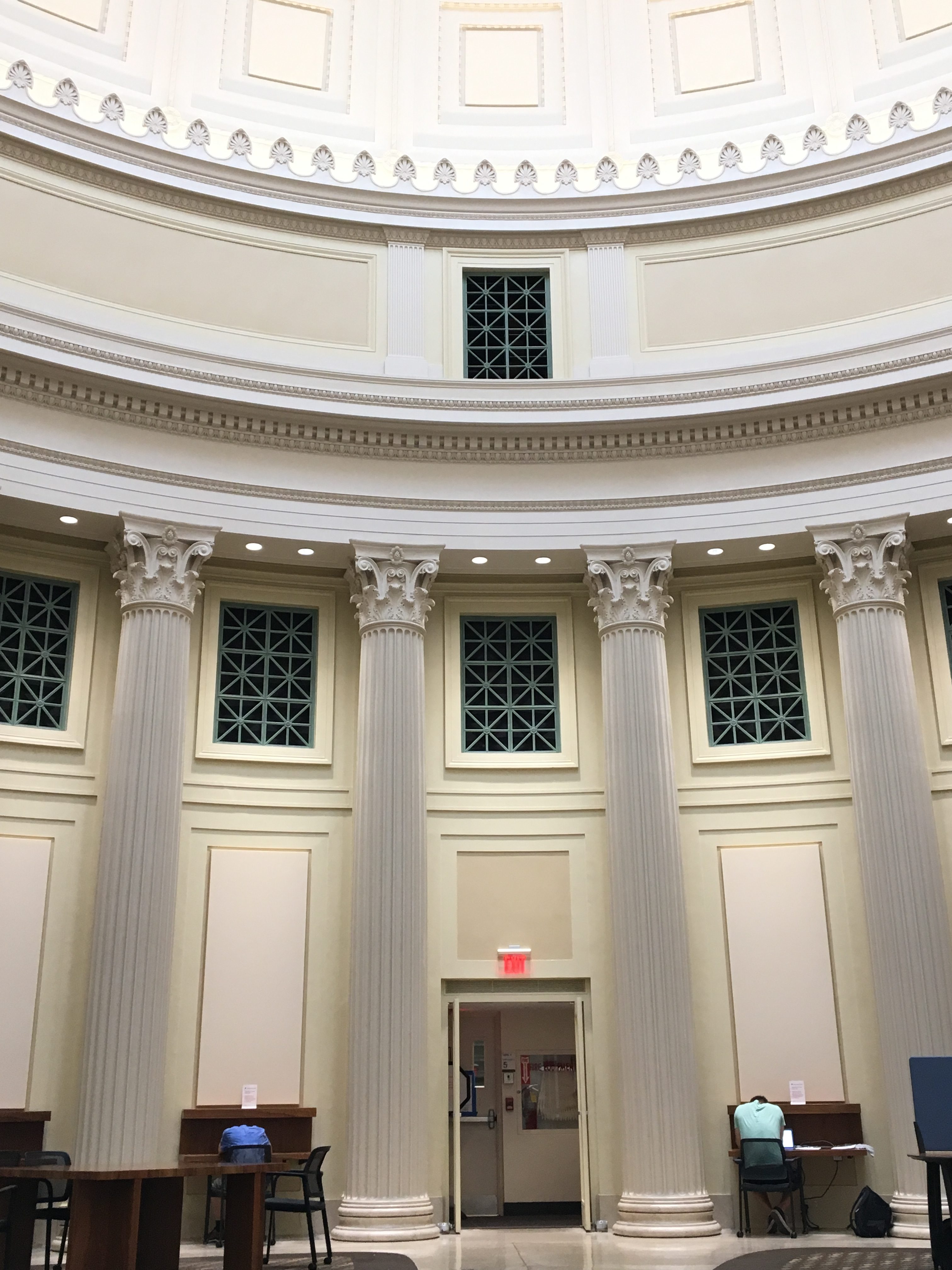 The side wall of Barker library, with the dome not visible. The wall is classical-looking and beige, with pillars supporting fancy moulding. At the bottom of the photo, an exit door and some study carrels are visible.