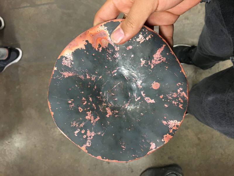 A nearly-flat circle of copper. It's black with soot from annealing in the furnace and in the middle, the imprint of a circle (soon to be the base) can be seen.