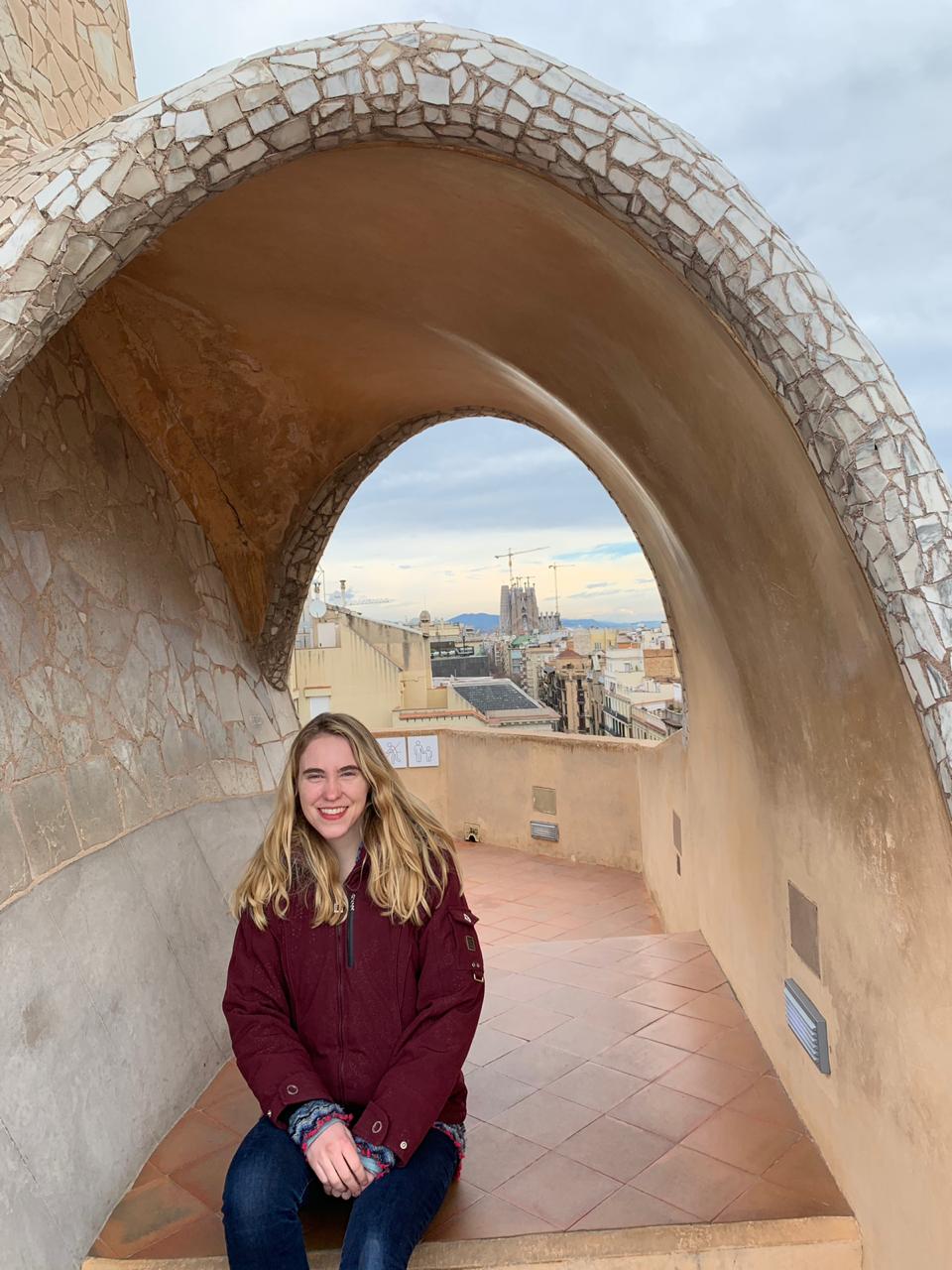 Me sitting under an arch on the roof of the Pedrera, with the Sagrada Familia in the background.