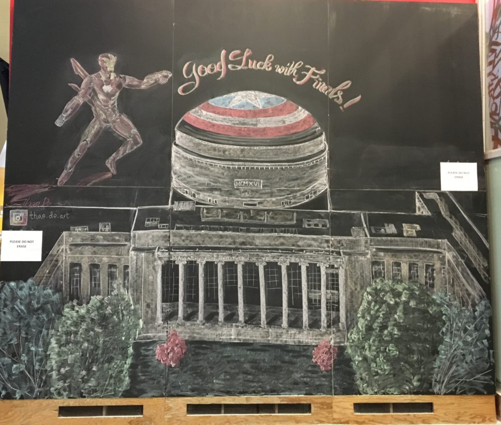 A very large blackboard inside the Stata Center. It is a detailed drawing of MIT's Killian Court, lobby 10, and the big dome. The dome is covered in Captain America's shield. Above it, Iron Man flies next to the words "Good Luck with Finals!"