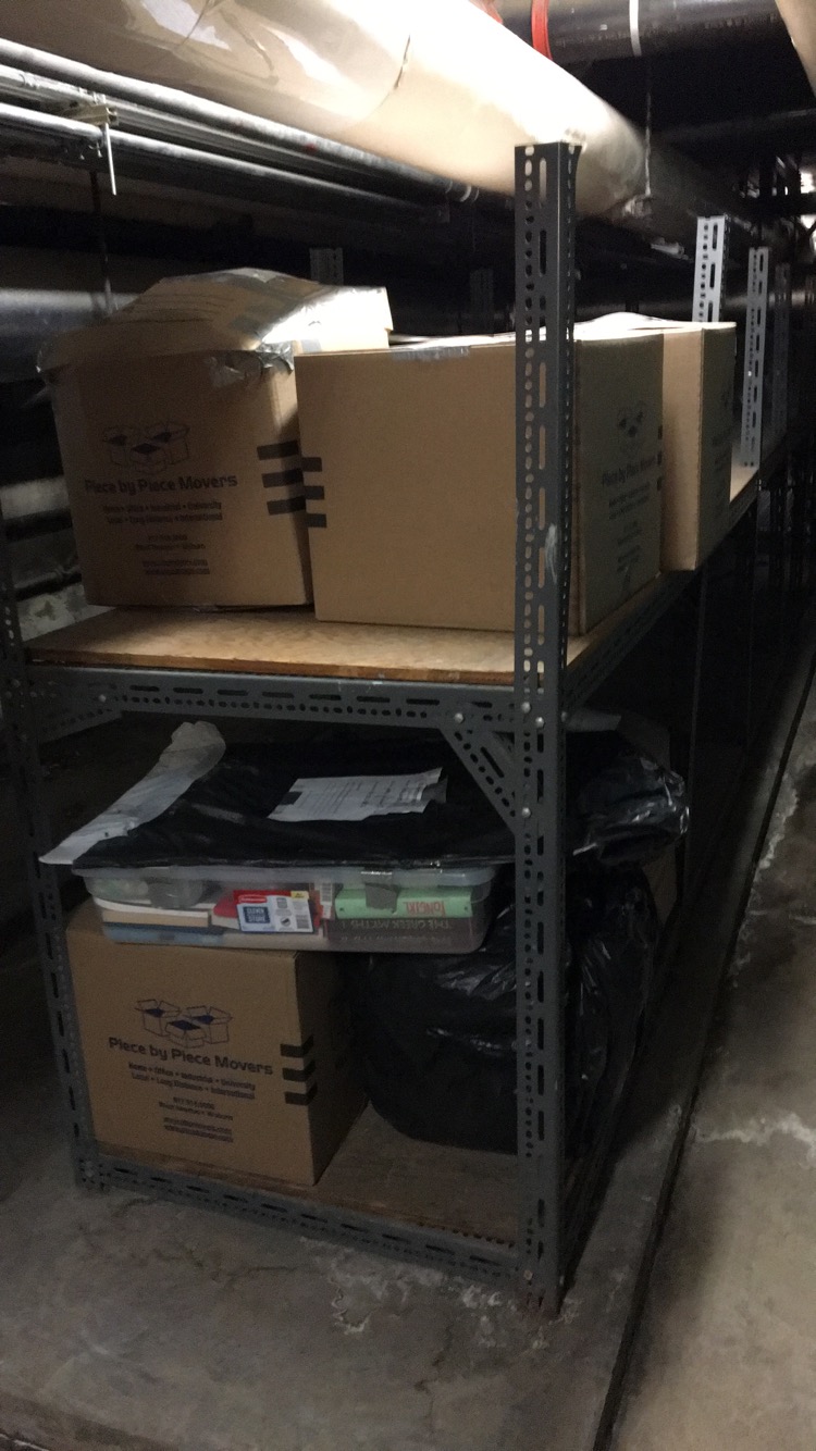 A metal and wood basement shelf with eight cardboard boxes on it.