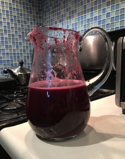 A large glass pitcher full of dark purple blueberry lemonade.