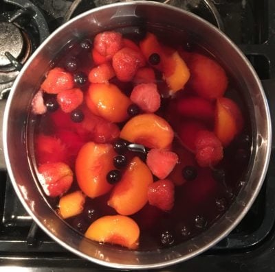 A pot full of boiling kompot (many different types of fruit in reddish, clear syrup).