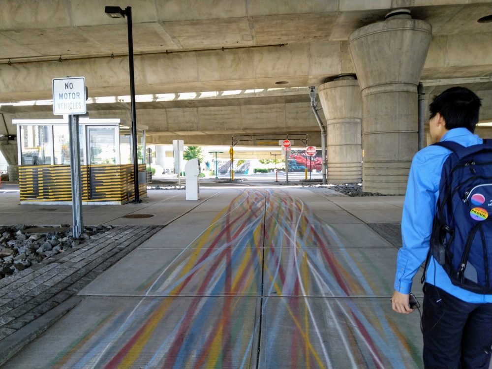 more colorful lines weaving into each other as the sidewalk widens to a path under the highway.