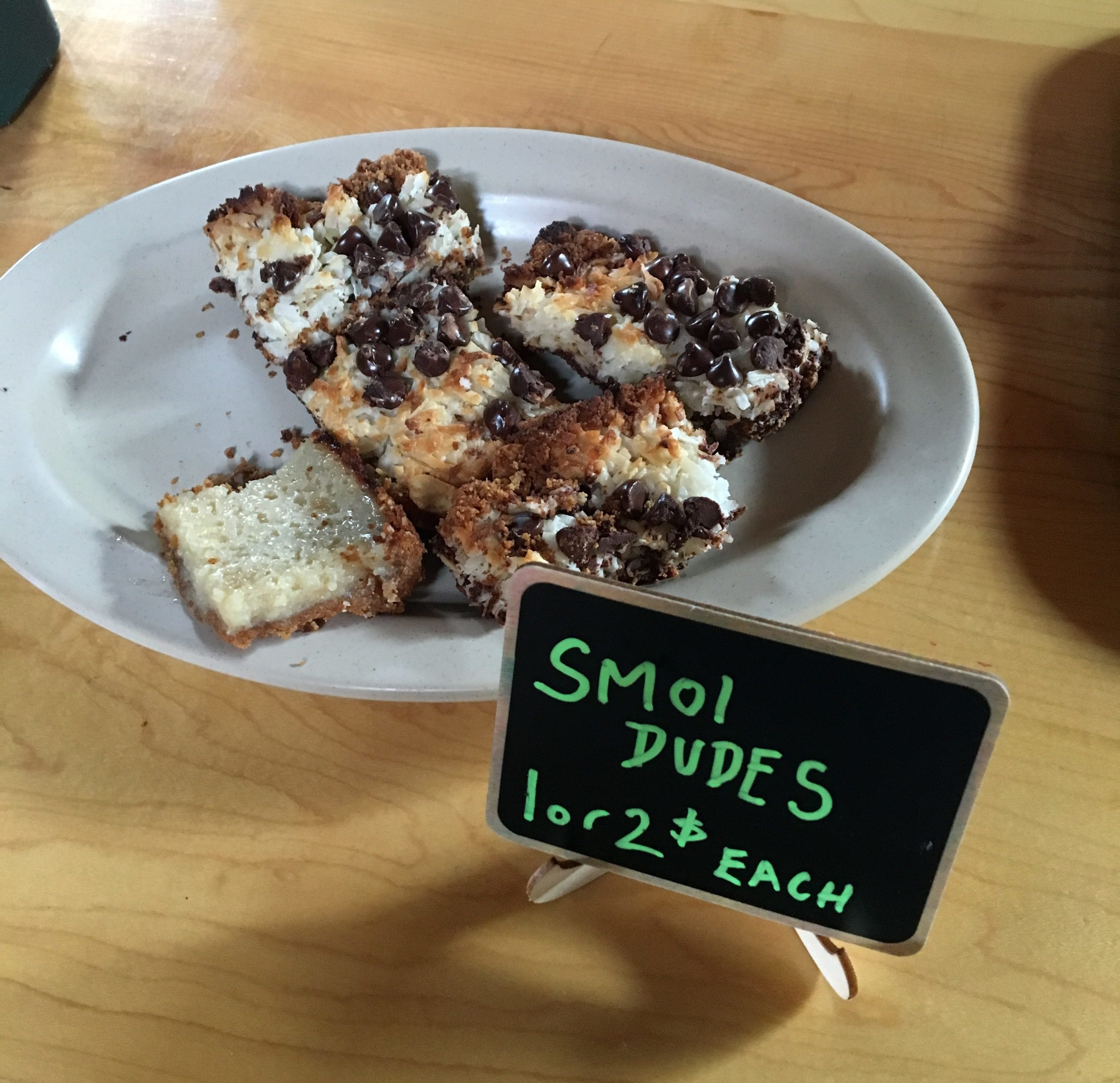 A plate of brownies on sale in a restaurant. A small sign proclaims them "SMOL DUDES: 1 or 2$ each".