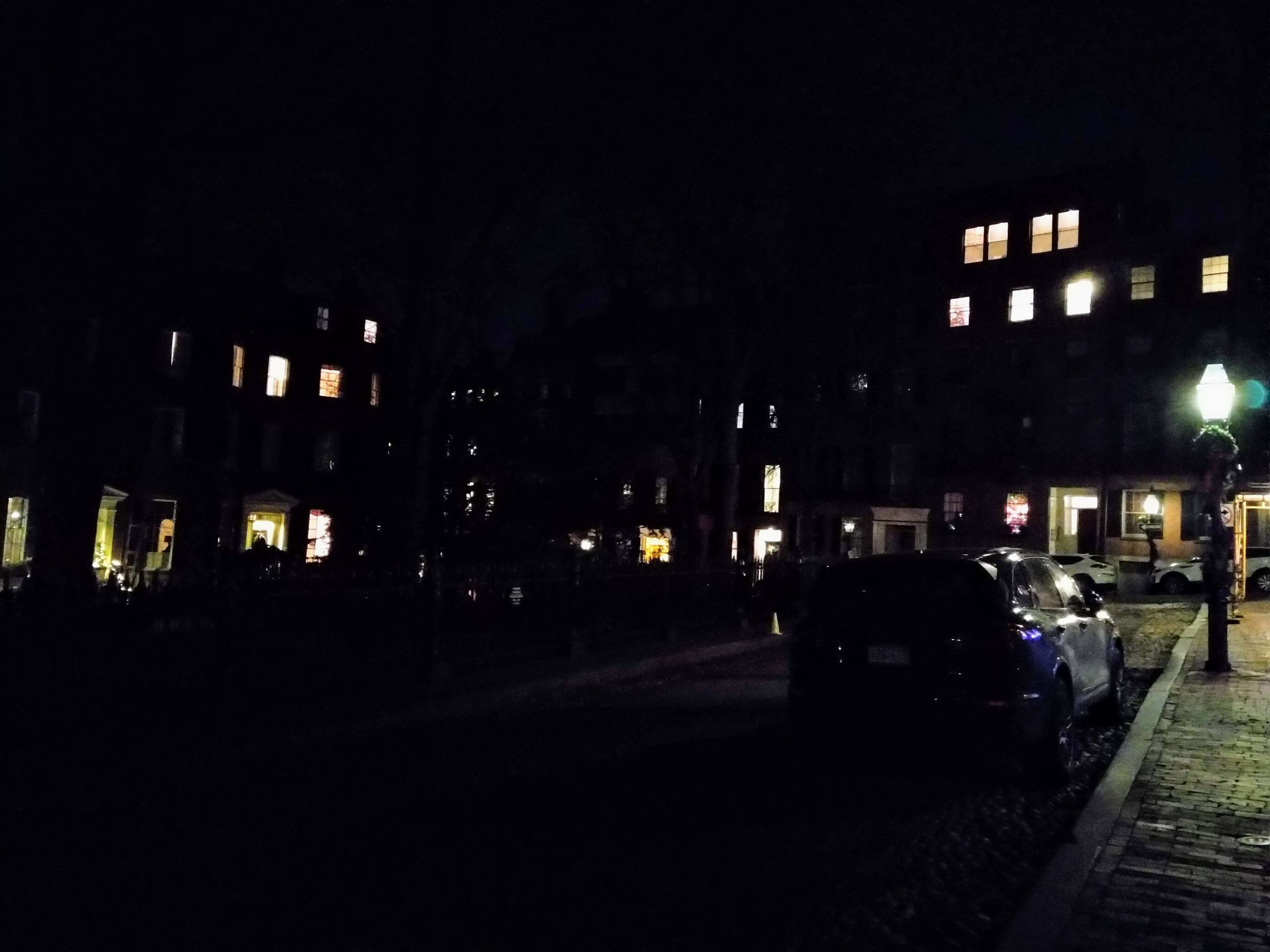 a dimly lit picture of the neighborhood. visible are windows in the distance, a car, and a lamppost.