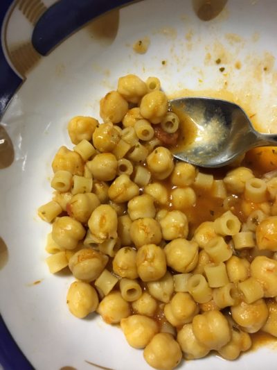 A white bowl with a spoon and chickpeas, pasta, and tomato sauce.