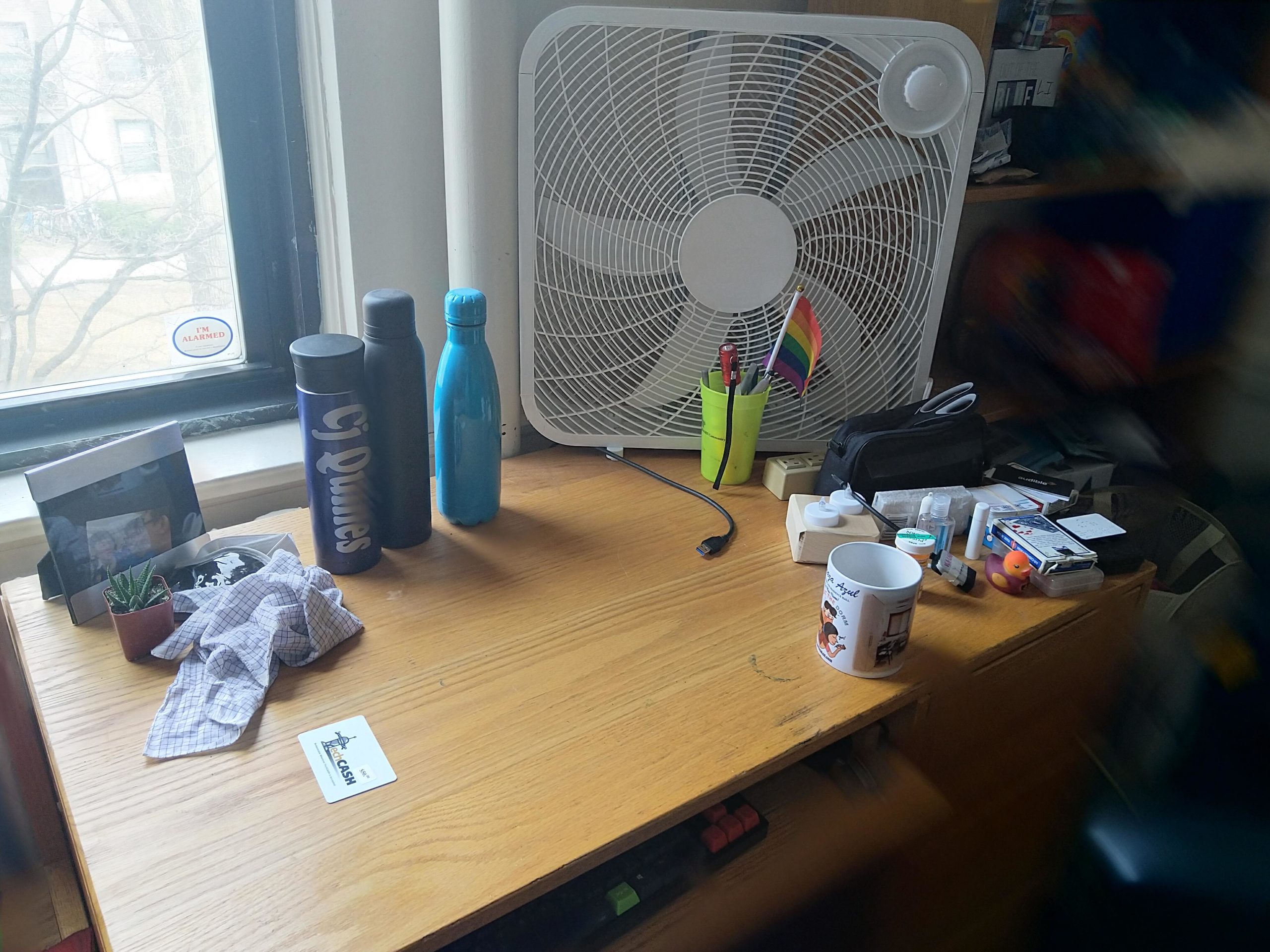 my desk. there’s a box fan, three water bottles, a mug, a keyboard.