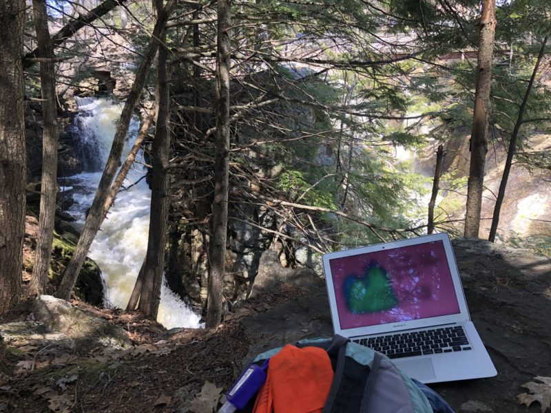 a picture of a laptop and a backpack next to a waterfall