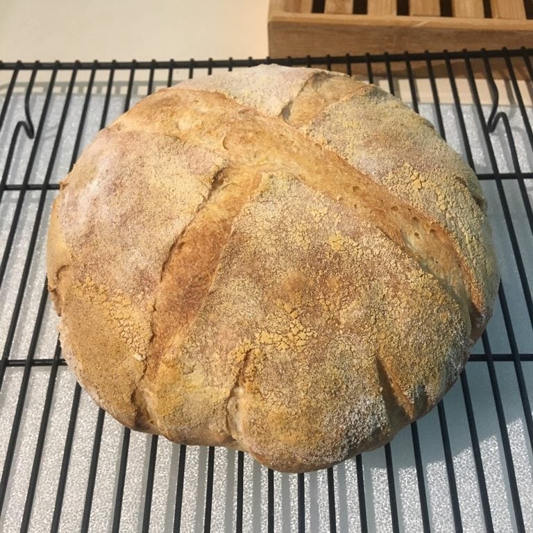 A loaf of sourdough bread I baked. It's round and light golden brown, with a number of small slashes around the sides.