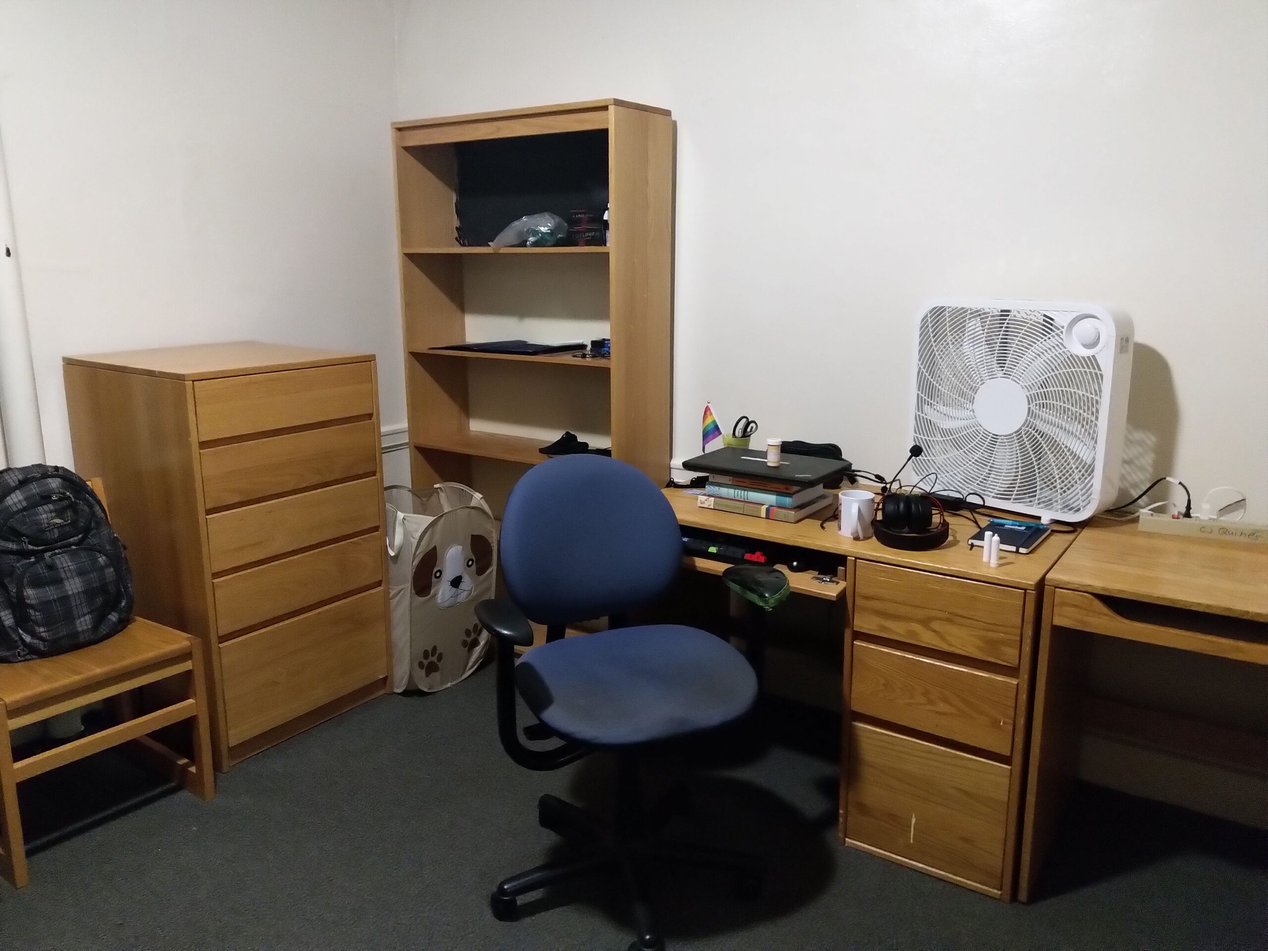 two tables next to each other. one has my laptop, a mug, my keyboard, mouse, a box fun. a cabinet to the left is pretty empty. an office chair is beside the desk.