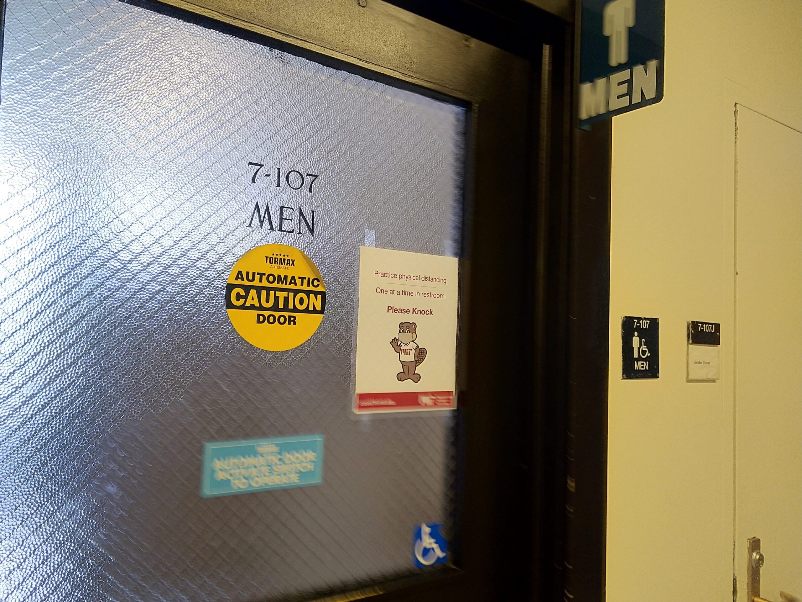 a bathroom, 7-107, with a sign saying "Practice physical distancing", "One person at a time in the restroom", "Please Knock"