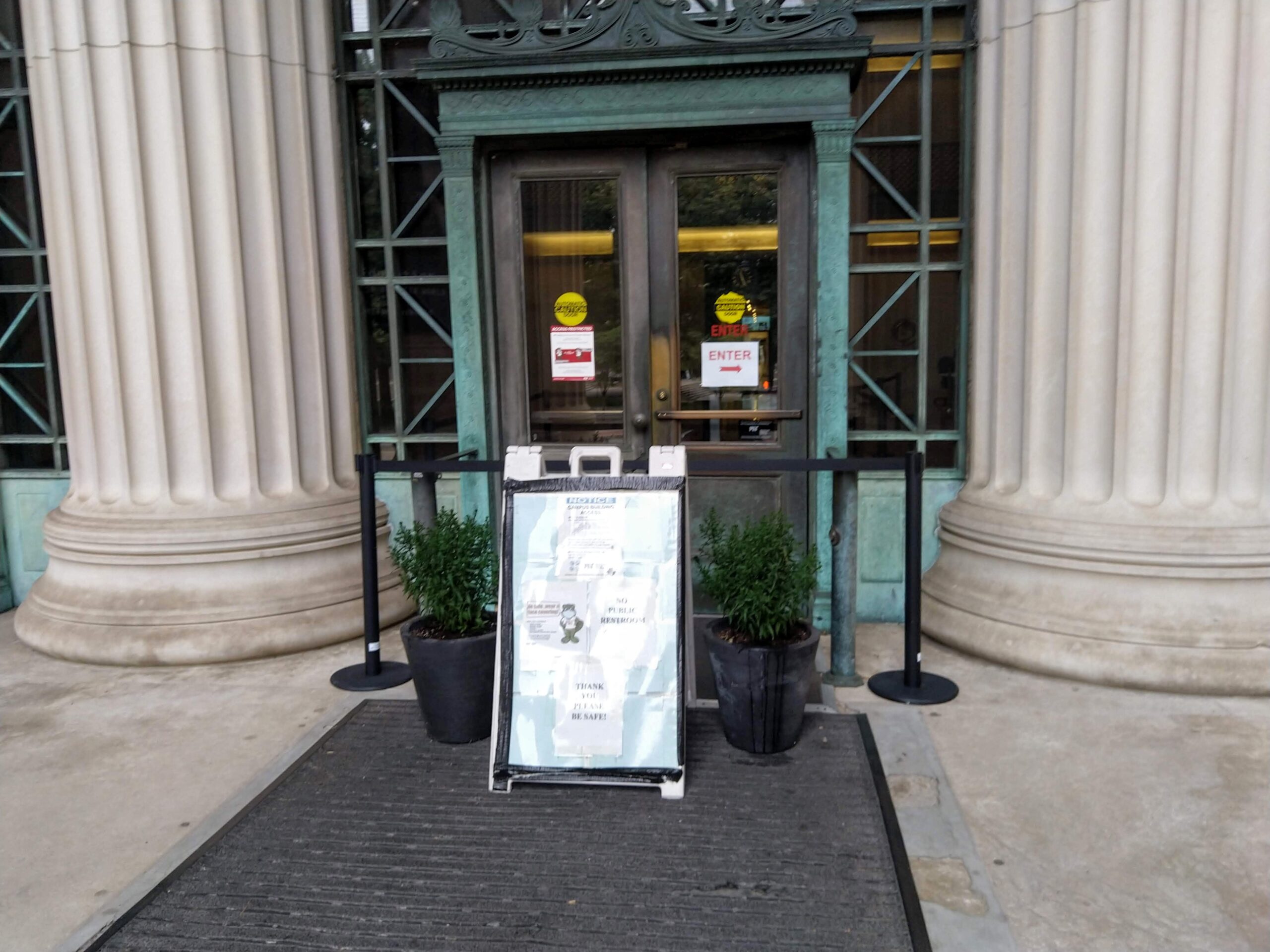 the door going into lobby 7, surrounded by two pillars, with stanchions, plants, and a sign blocking it