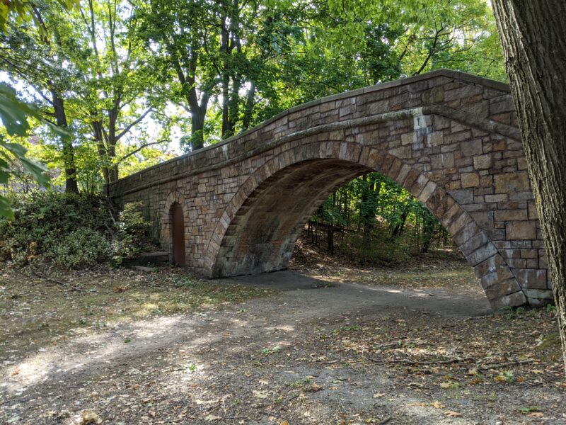 a stone bridge over an unpaved path in a park