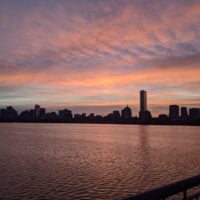 a spot of light shines up into pink clouds as the sun rises over boston