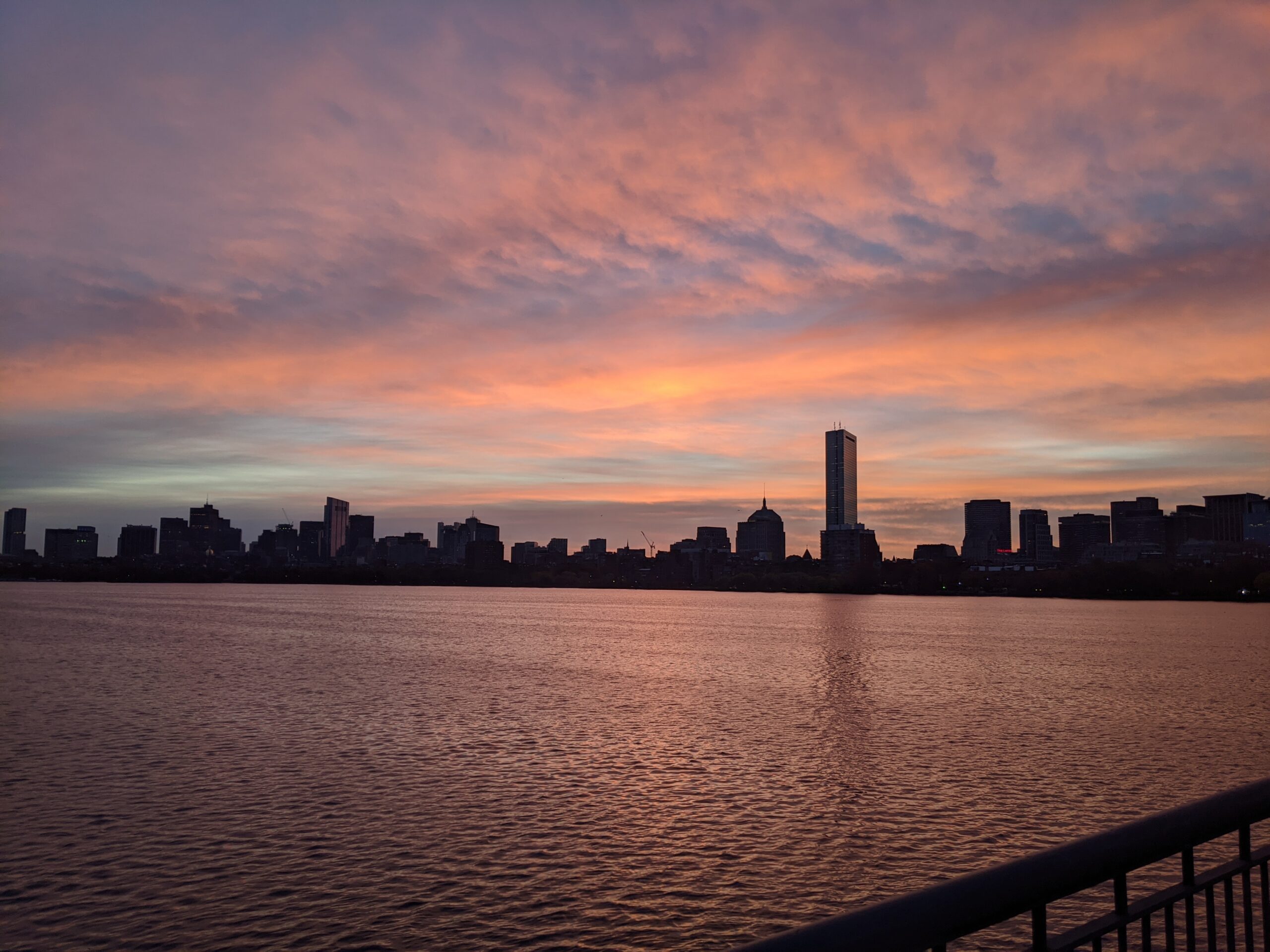 a spot of light shines up into pink clouds as the sun rises over boston