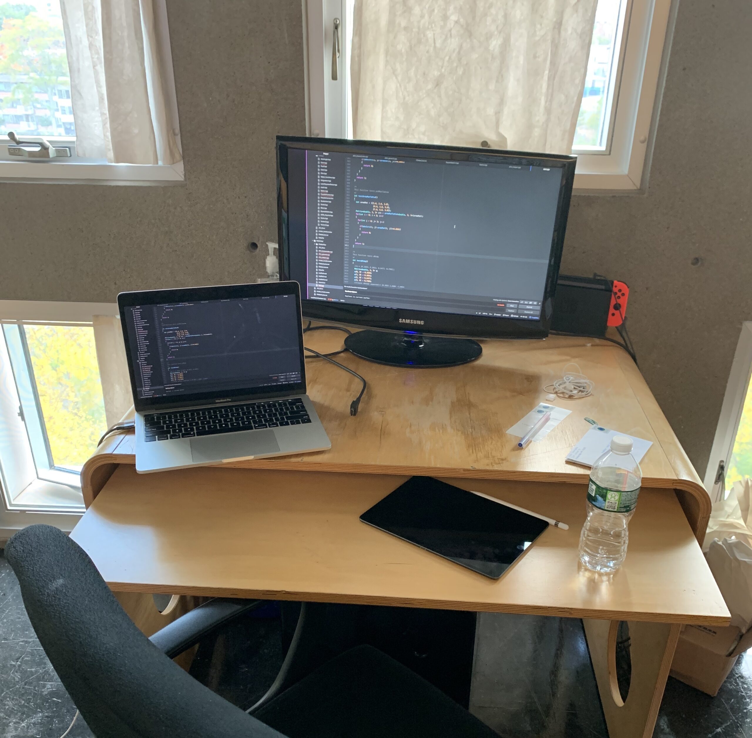 normal desk with a monitor, laptop, ipad, and switch in the background