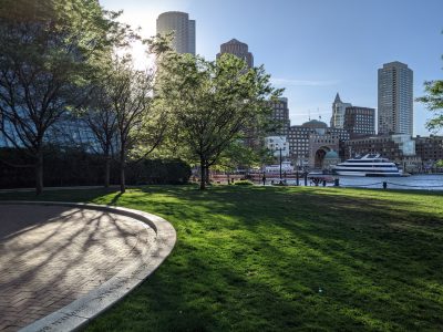 picture of green space in front of water and boston skyline at sunset