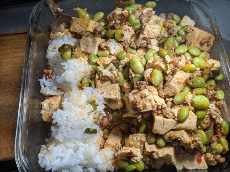 tupperware containing rice on the left, covered with tofu and edamame beans on the right