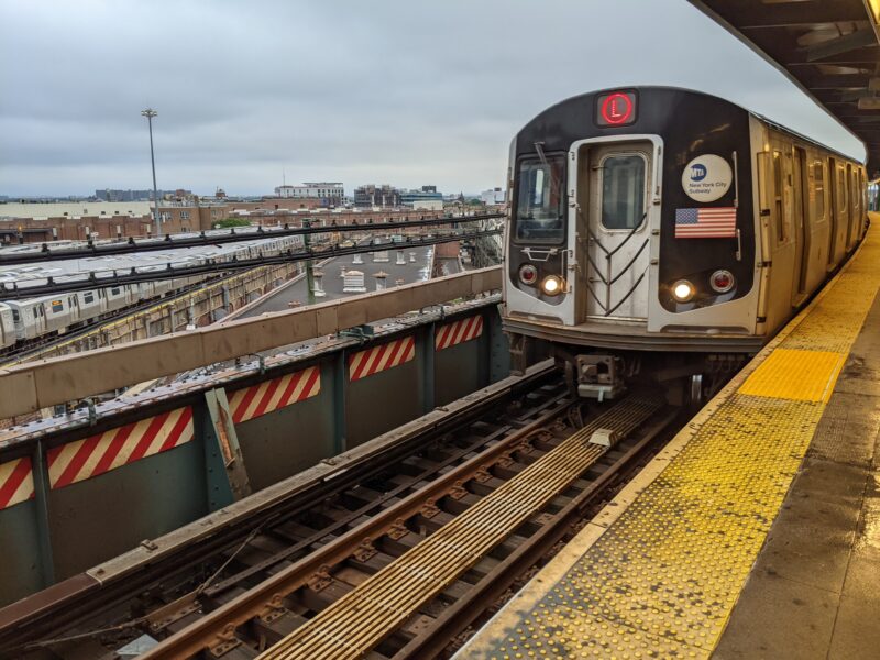 L train pulling into an elevated station in front of a train yard