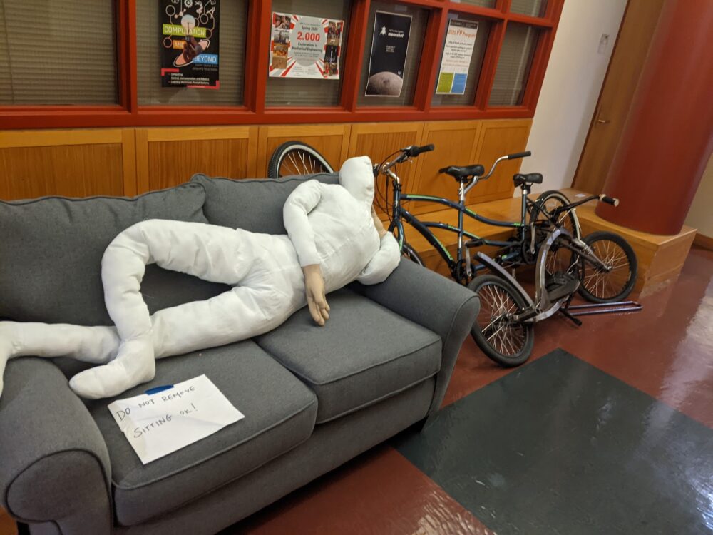 mannequin on a couch with sign reading "do not remove. sitting ok!" with bikes behind it