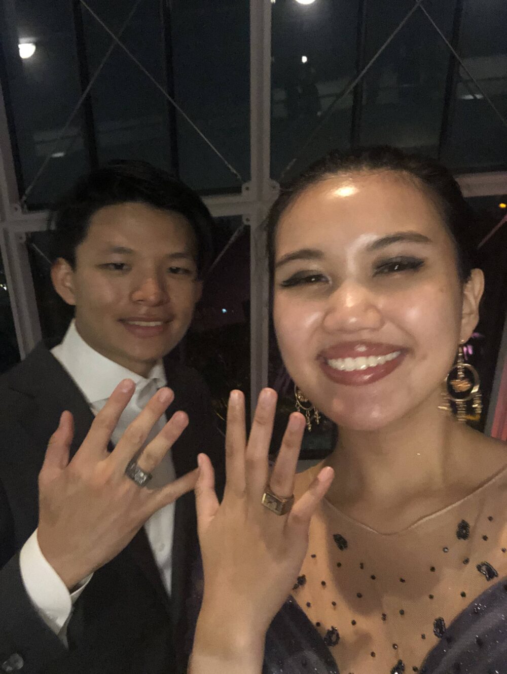 a man and woman smiling while showing off their rings