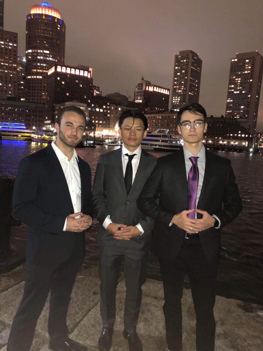 three men (aidan, aiden, and raymond) posing in front of the waterfront in their suits