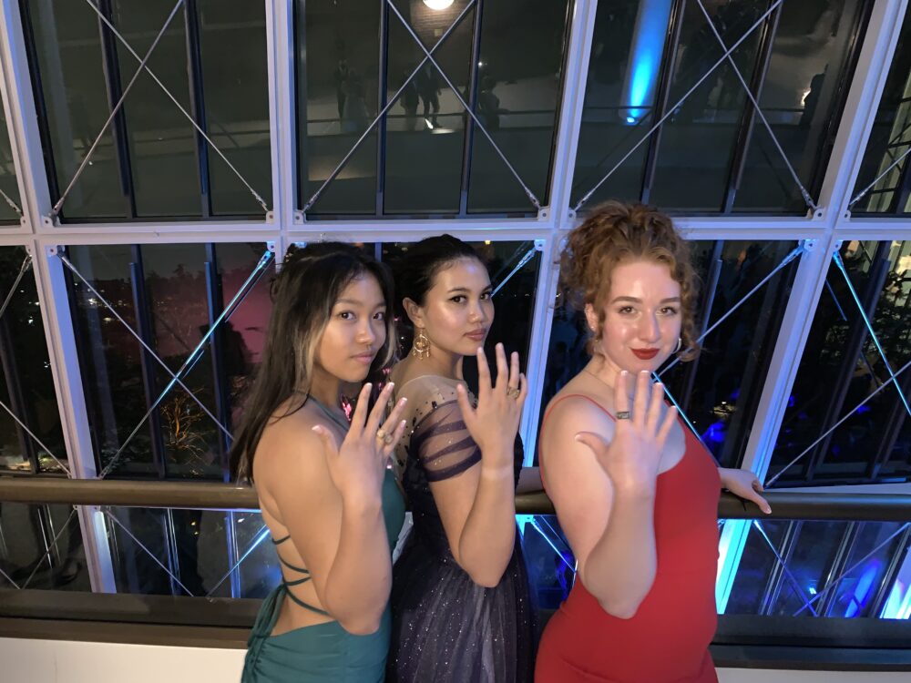 three women in dresses with their hands up showing off their rings