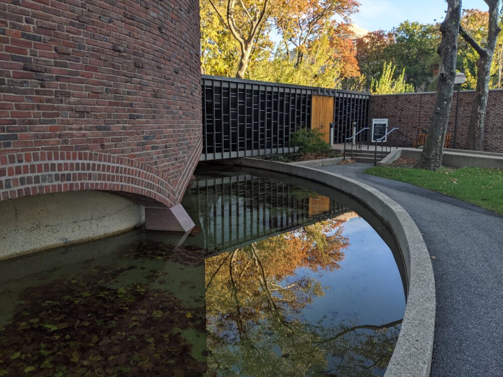 fall trees reflected against a moat around a brick building