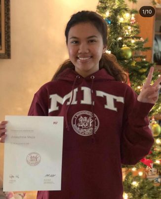 cami wearing an mit hoodie holding her mit acceptance letter and smiling with a peace sign in front of a christmas tree