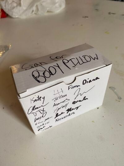 white paper box with "sign for body pillow" on one side and signatures on another side