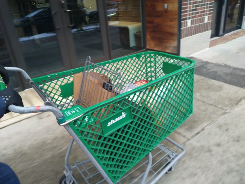 green shopping cart with "shaw's" being rolled along the sidewalk