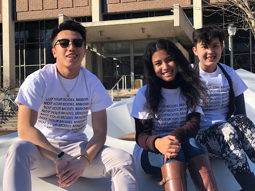 three college age students sitting outside posing in a shirt that reads 'not your model minority'