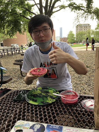 college age man giving a thumbs up and eating beet hummus on bread g