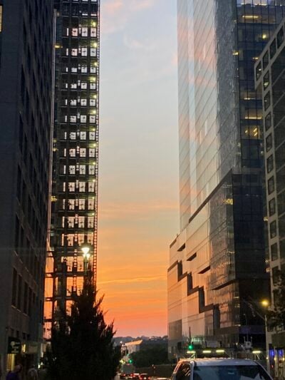A colorful sunset. It is framed by two buildings, both so tall that they go out of the frame. The sunset's colors reflect on the building on the right.
