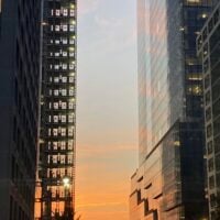 A colorful sunset. It is framed by two buildings, both so tall that they go…