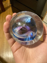 A paperweight. It is clear with blue, white, and purple swirls in the center.