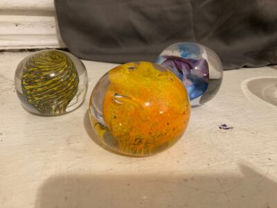 Three paperweights, all with clear glass outsides and interestingly-colored middles. One is an alternating yellow and blue spiral, one is a firey mix of yellow and orange, and one is a mishmash of blue, white, and purple.