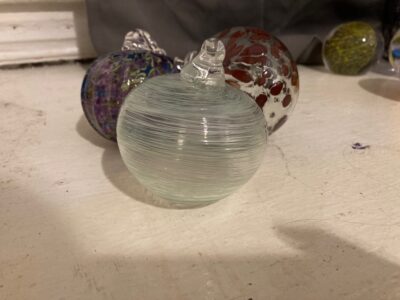 Three Christmas ornaments. One is a swirl of white and pale green, one is clear with big maroon spots, and one is a mishmash of purple, green, and blue, with ribs like a pumpkin.