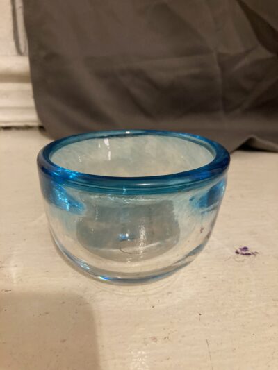 A small bowl. The rim of the bowl is a bright blue and it fades to clear.