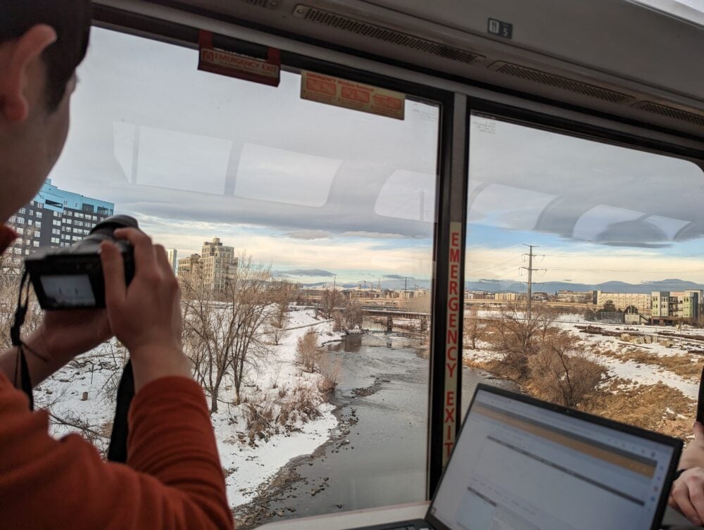 person taking a photo of a river with mountains in the distance