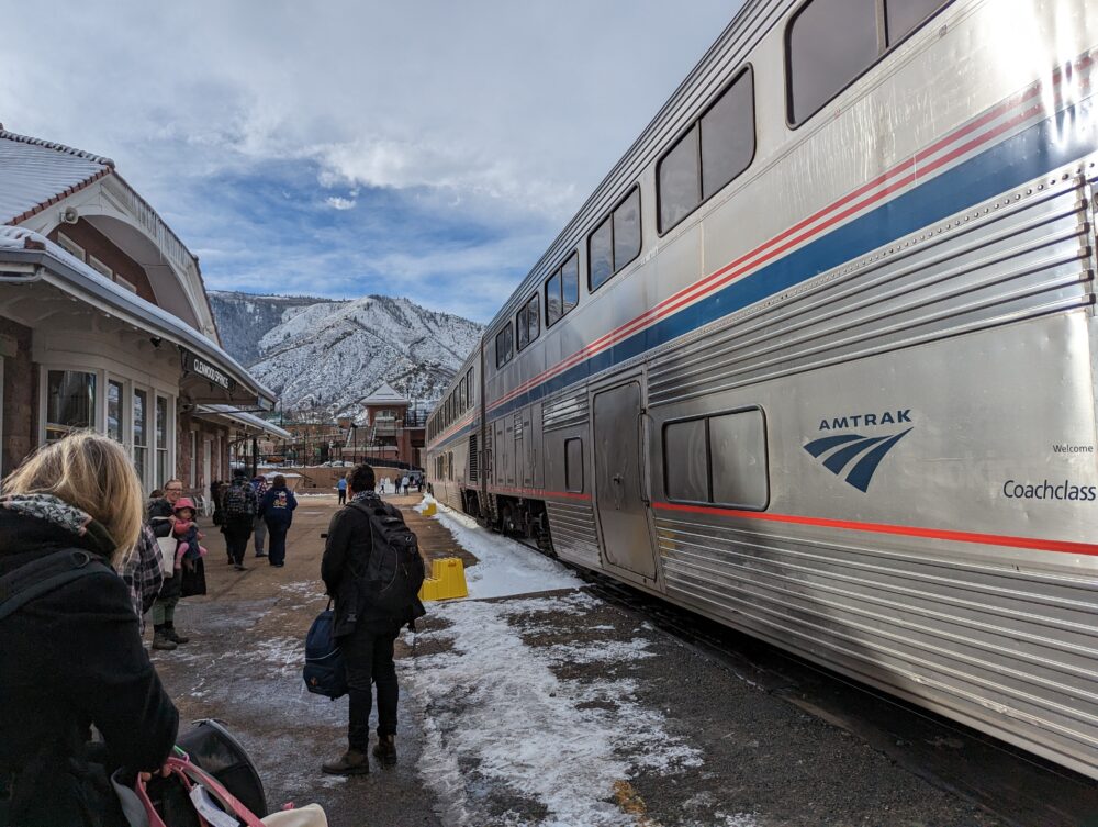 amtrak train next to station building, with mountain in the distance