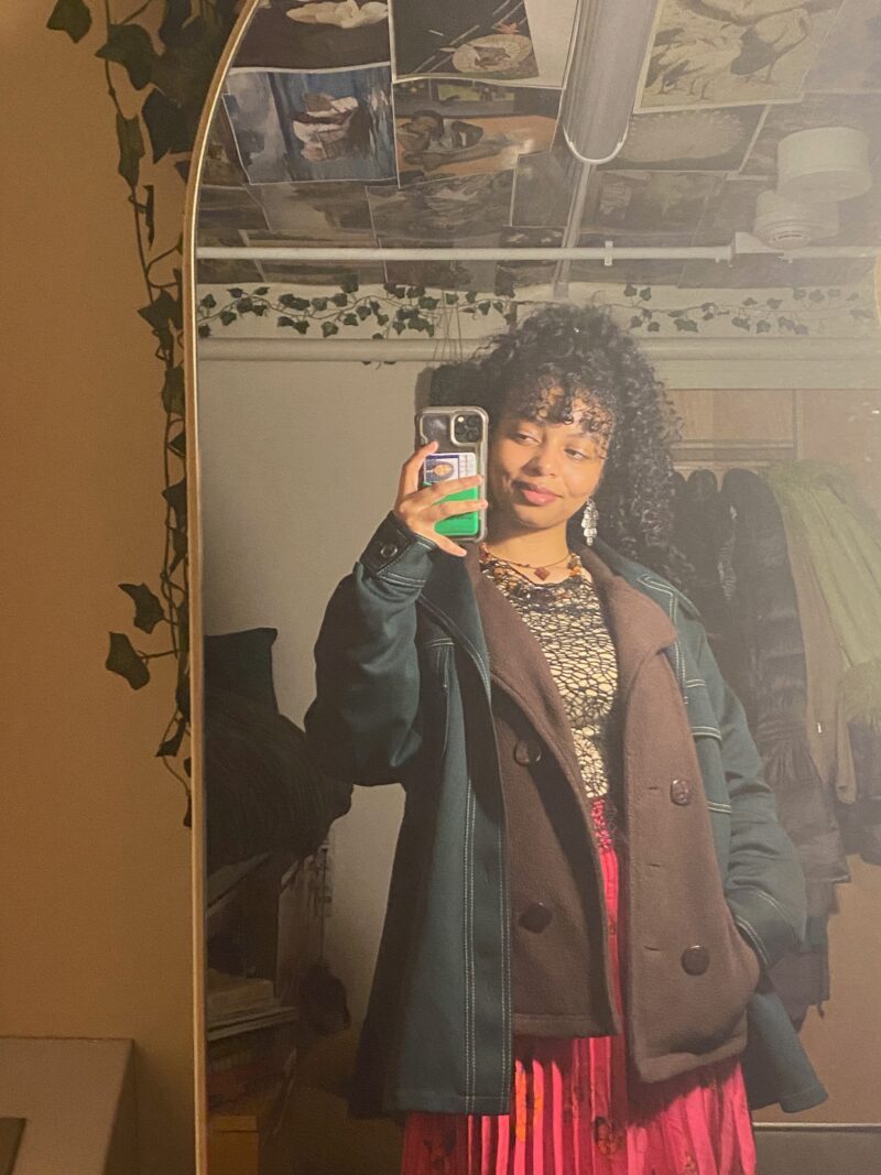 black woman wearing green jacket over a brown jacket with a pink skirt