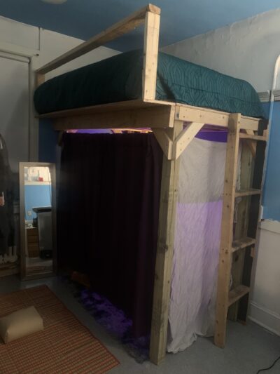lofted bed that I built with deep teal bedding, appended with an extension to fit a larger mattress