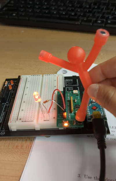 stick figure shaped fridge magnet held above an electronic circuit, where one LED is lit