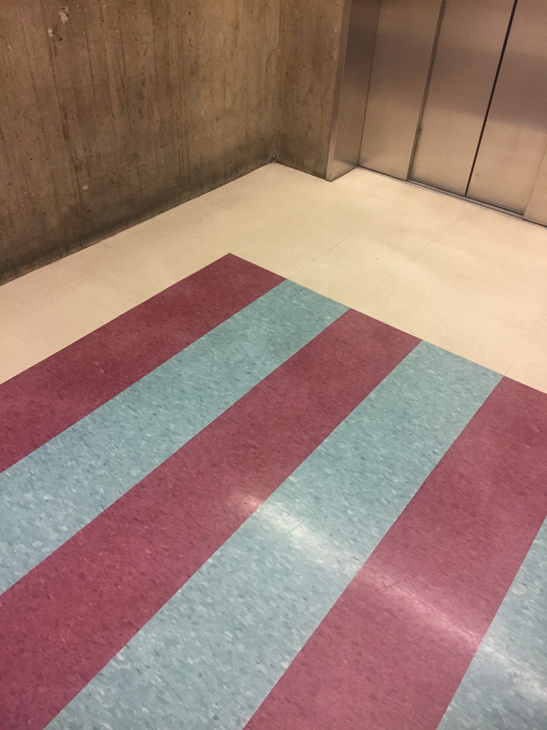 a picture of an elevator, concrete walls, blue and red striped floors