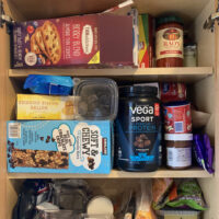 The cabinet with the doors open. Lots of different food packagings are stacked on the…